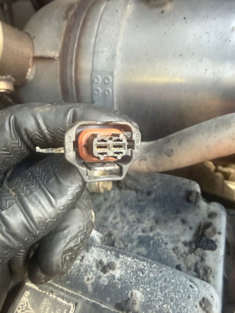 Close-up of a gloved hand holding a car engine electrical connector